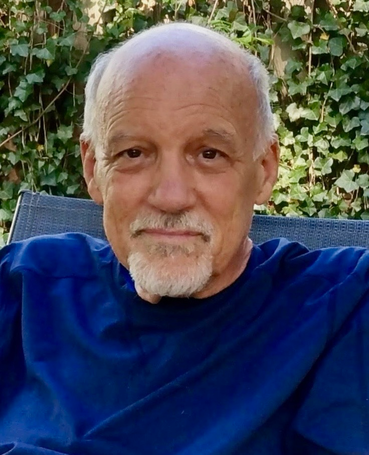 James Revels, seated outdoors in a blue shirt with ivy behind him